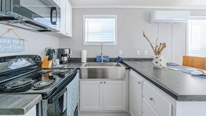 A kitchen with a stove, sink, cabinets, and a window.