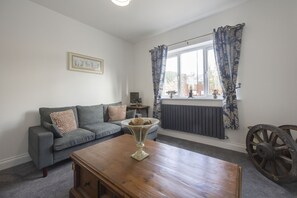 En stue med en grå sofa, et træbord, en radiator og et vindue med blå gardiner.