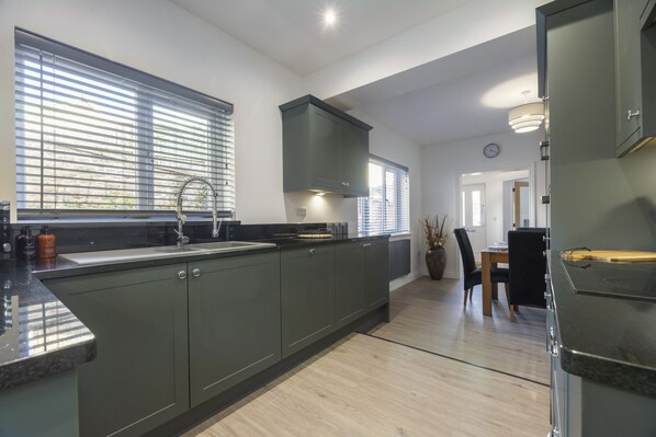 Una cocina moderna con armarios oscuros, una isla grande y una zona de comedor con mesa y sillas.