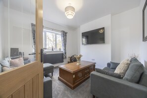 A modern living room with a sofa, a wooden coffee table, and a television mounted on the wall. - Beautiful 3-Bed Home with Hot Tub in Ross-on-Wye (Ross-on-Wye)