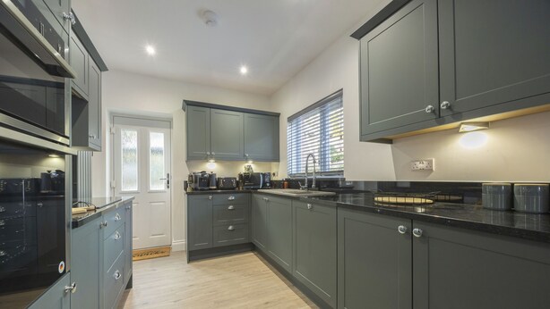 A modern kitchen with grey cabinets, a black countertop, and a wooden floor.