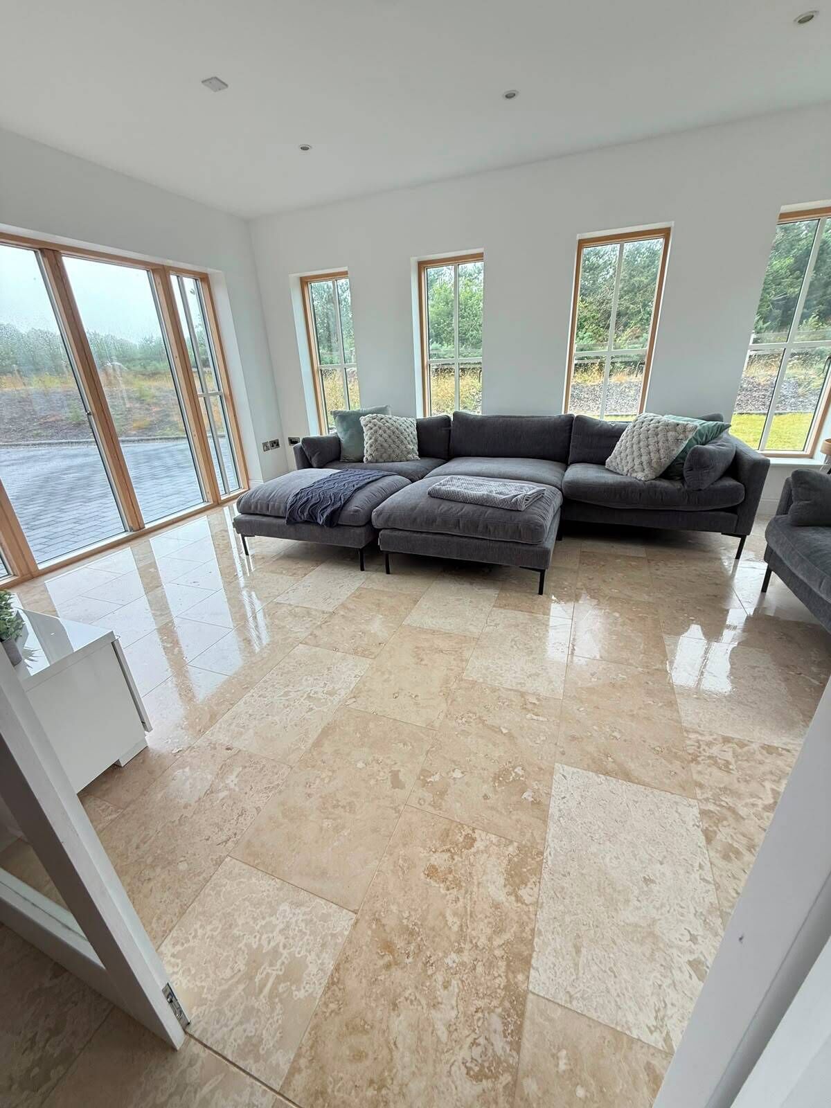 A spacious living room with a large sectional sofa, a glass door leading to a view of a body of water, and a tiled floor.