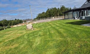 A well-maintained lawn with a stone feature, a white fence, and a modern building with large windows. - A large 4 bed family home to make great memories in the West Coast of Ireland. (Westport)