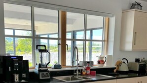 A modern kitchen with a large window, a coffee machine, a blender, and a kettle. - A large 4 bed family home to make great memories in the West Coast of Ireland. (Westport)