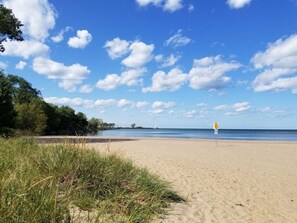A beach with a clear sky, a lighthouse in the distance, and a lifeguard sign on the sand. - Beach Community-2 Homes-7 bdrms/4 bths (Huron)