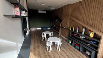 Un interior moderno con una zona de comedor que presenta mesas y sillas redondas blancas, suelo de madera y estanterías empotradas con juguetes y libros.