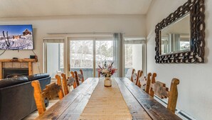 Een eetkamer met een lange houten tafel, houten stoelen, een open haard, een televisie en een grote spiegel.