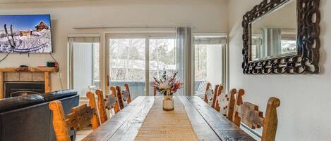 A dining room with a long wooden table, wooden chairs, a fireplace, a TV, and a large mirror.
