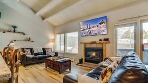 Een gezellige woonkamer met een open haard, houten meubels en een grote tv aan de muur.