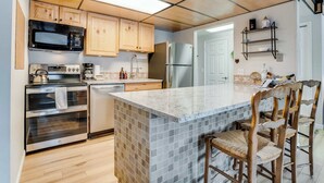 Een moderne keuken met houten kastjes, een ingebouwde magnetron, een roestvrijstalen koelkast en een groot kookeiland met barkrukken.