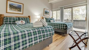 Een kamer met twee bedden, elk met beddengoed in het groen en wit geruit, een houten stoel en een raam met uitzicht op bomen.