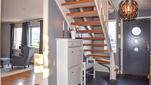Ein modernes Interieur mit einer Holztreppe, einem weißen Schrank, einem grauen Sessel und einer Tür mit rundem Fenster.