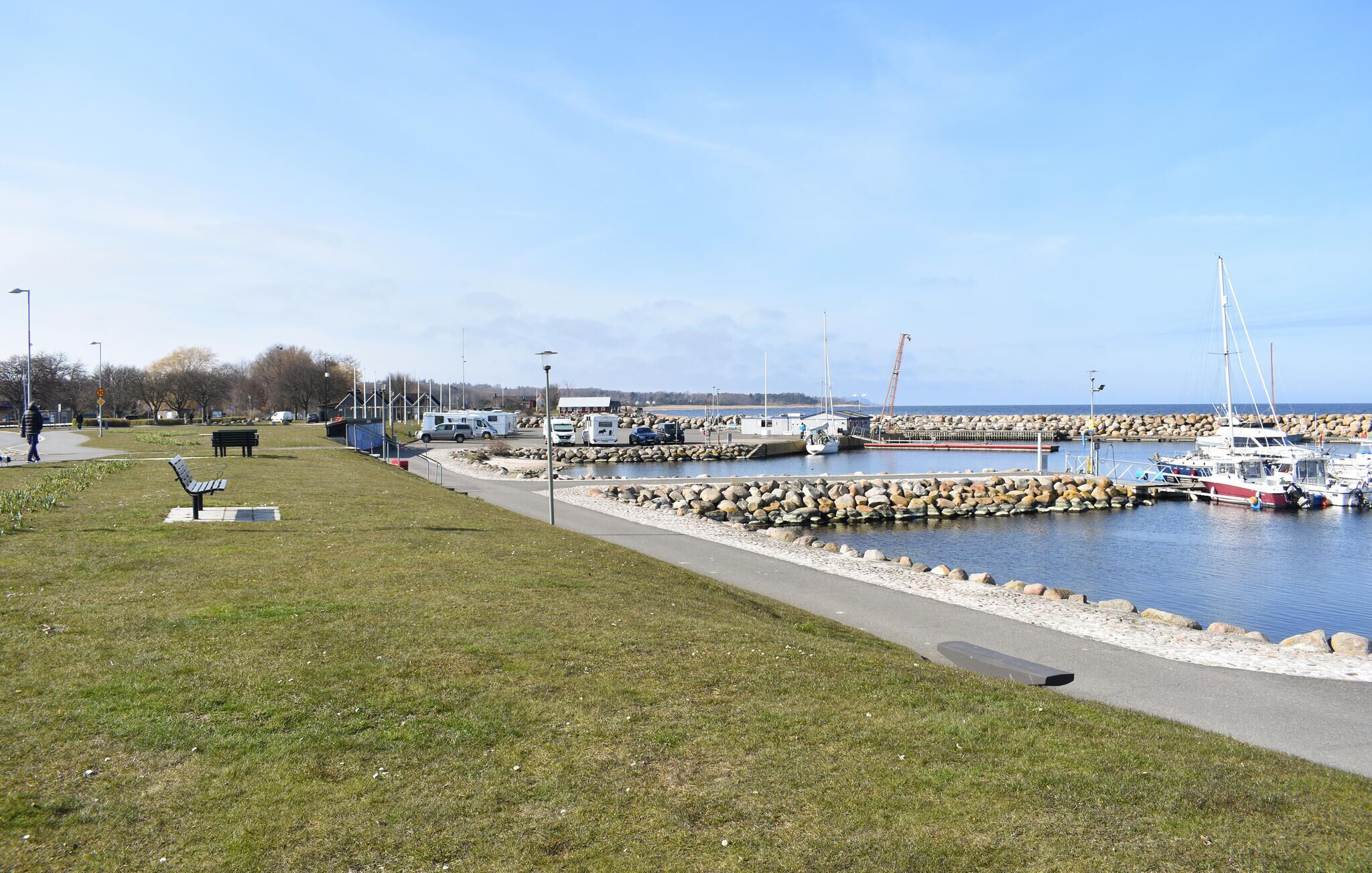 A marina with boats docked, a walking path, and a grassy area with benches.