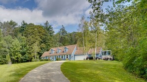 Una grande casa a due piani con un vialetto che conduce all'ingresso, immersa nel verde e circondata da alberi.