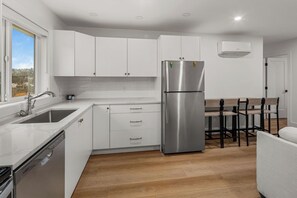 Eine moderne Küche mit weißen Schränken, Edelstahlgeräten und einem Essbereich aus Holz.