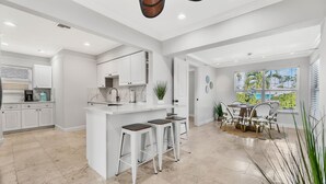 A modern kitchen with white cabinetry, a central island with stools, and a dining area with a table and chairs. - Waterfront Oasis • Pool • Ocean Access. near beach.near golf.pet friendly (Pompano Beach)