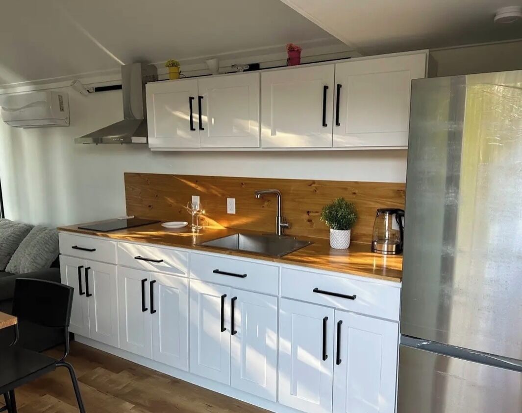A modern kitchen with white cabinets, a wooden countertop, and a stainless steel refrigerator.