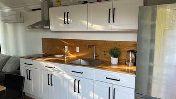 A modern kitchen with white cabinets, a wooden countertop, and a stainless steel refrigerator.