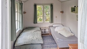 A small, cozy room with two beds, a window with curtains, a small table, and a shelf with a picture. - 2 bedroom amazing home in Fagerhult (Fagerhult)
