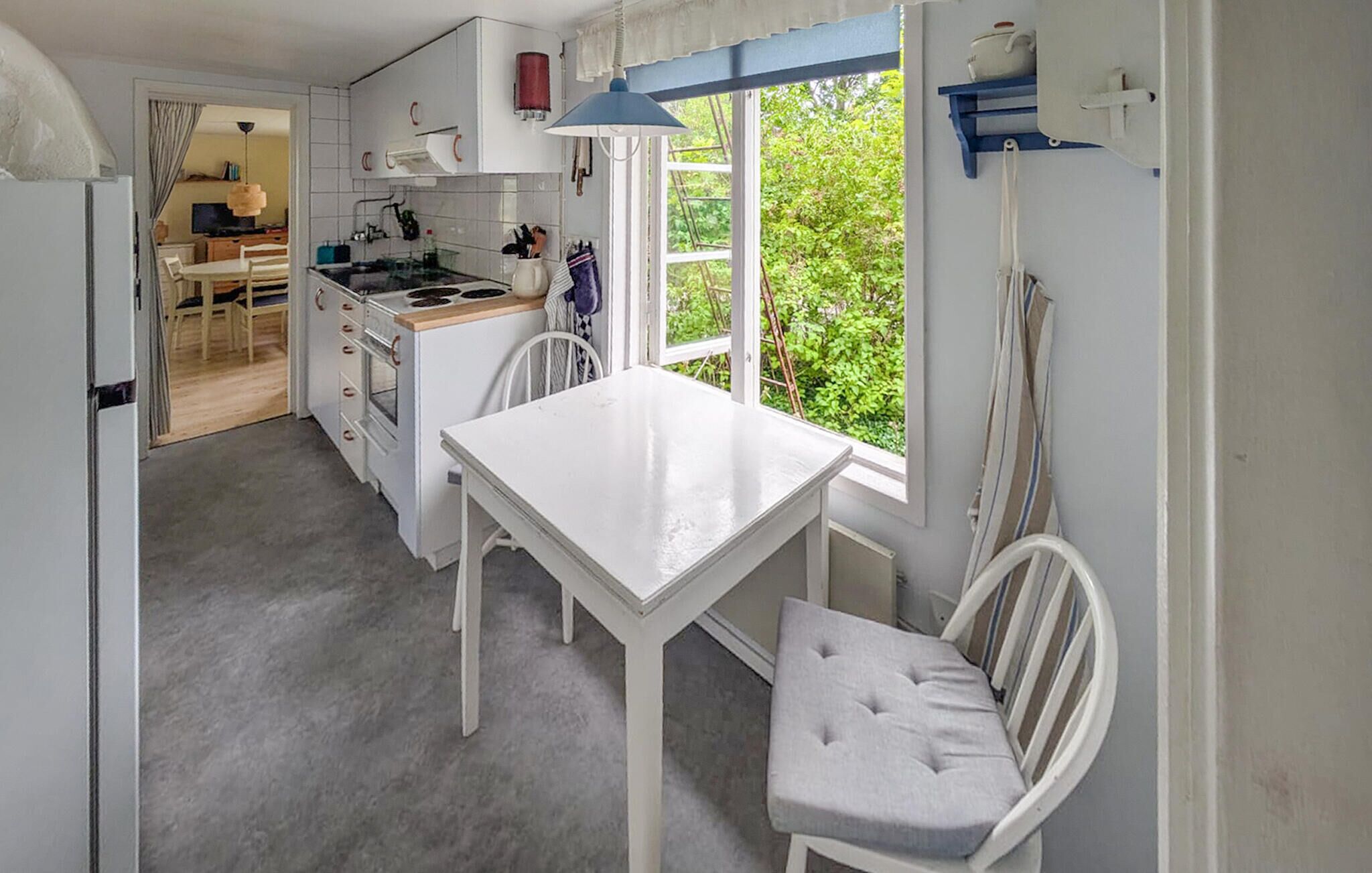 A compact kitchen with a white table and chairs, a stove, and a window with a view of greenery.