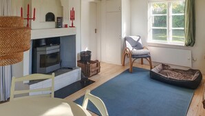 A cozy living room with a fireplace, a comfortable chair, a pet bed, and a large window with curtains. - 2 bedroom amazing home in Fagerhult (Fagerhult)