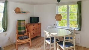 A cozy room with a wooden floor, a round dining table with chairs, a television on a wooden cabinet, and a window with green curtains. - 2 bedroom amazing home in Fagerhult (Fagerhult)