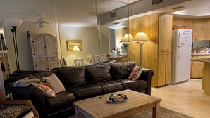 A living room with a brown leather sofa, a wooden coffee table, and a dining area with wooden cabinets and a refrigerator. - Riverfront 2-bedroom townhome in peaceful Homosassa with AC/Heat, Pool (Homosassa)
