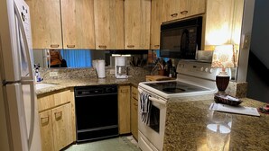 A kitchen with wooden cabinets, a dishwasher, a stove, a microwave, and a coffee maker. - Riverfront 2-bedroom townhome in peaceful Homosassa with AC/Heat, Pool (Homosassa)
