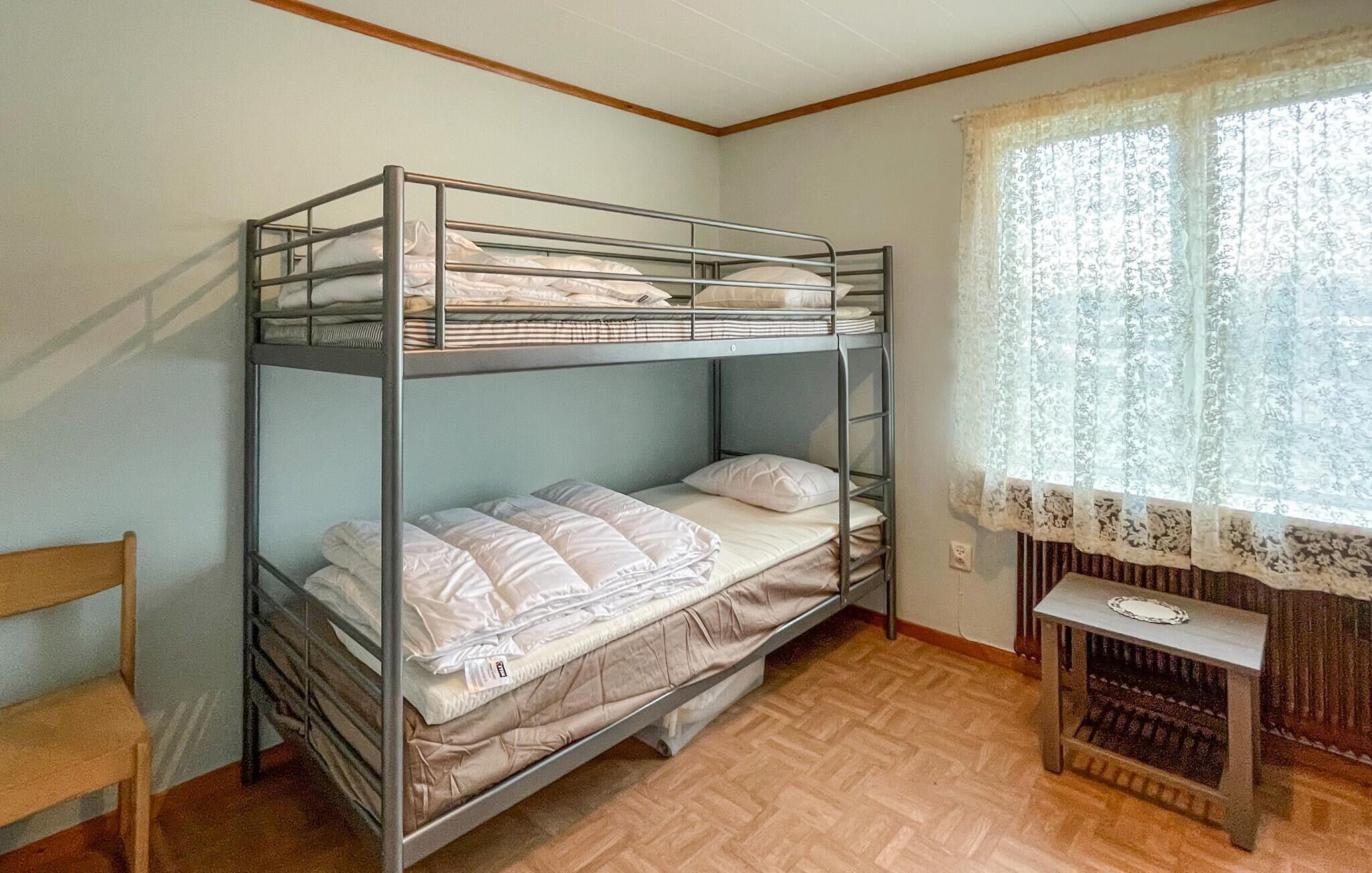 A bunk bed room with a small table and a window with lace curtains.