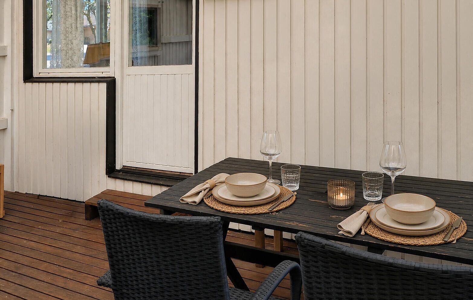Een eettafel gedekt met borden, kommen, glazen en bestek op een houten terras.
