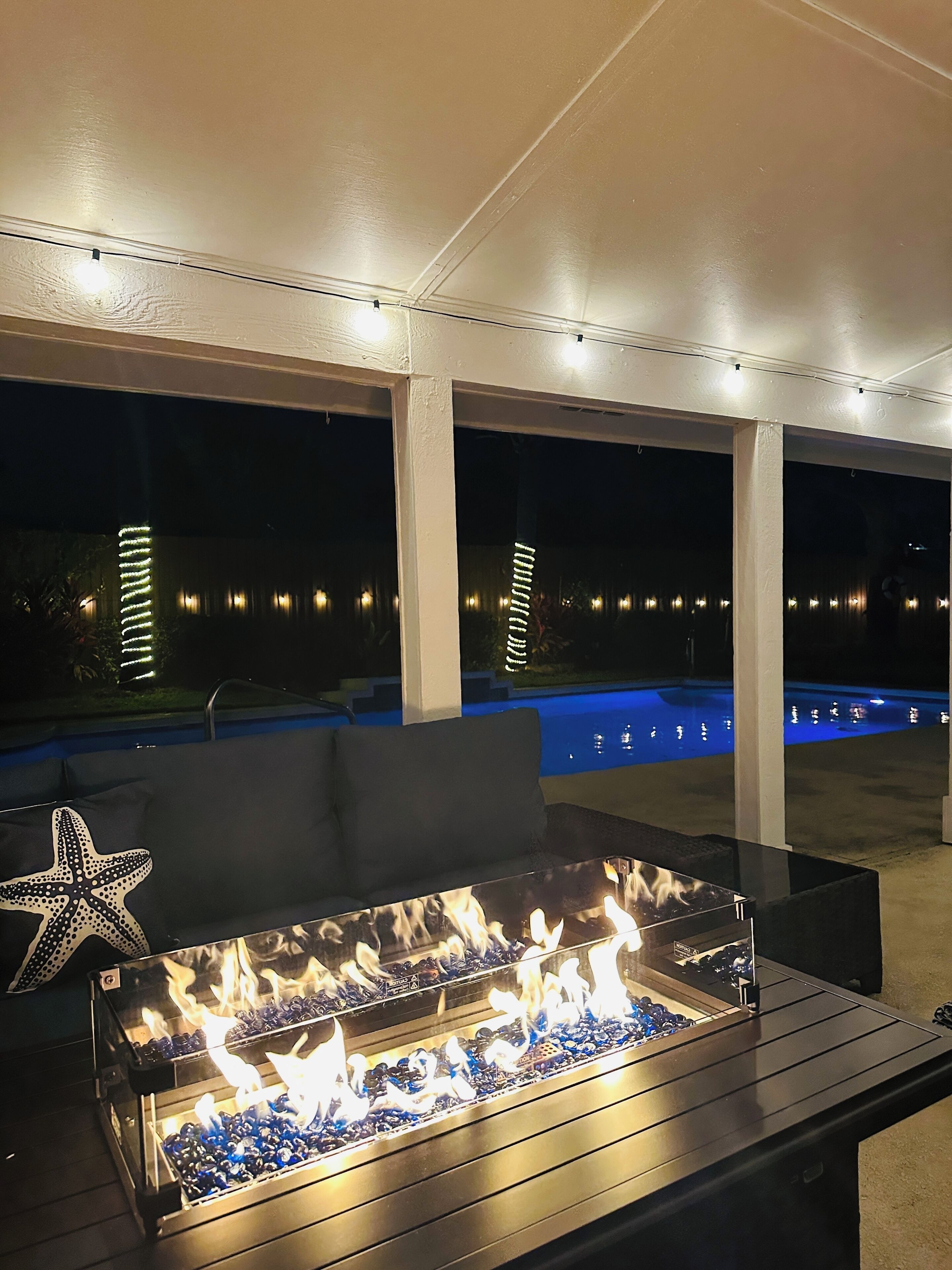 Un espacio de estar al aire libre con una chimenea y una piscina al fondo.