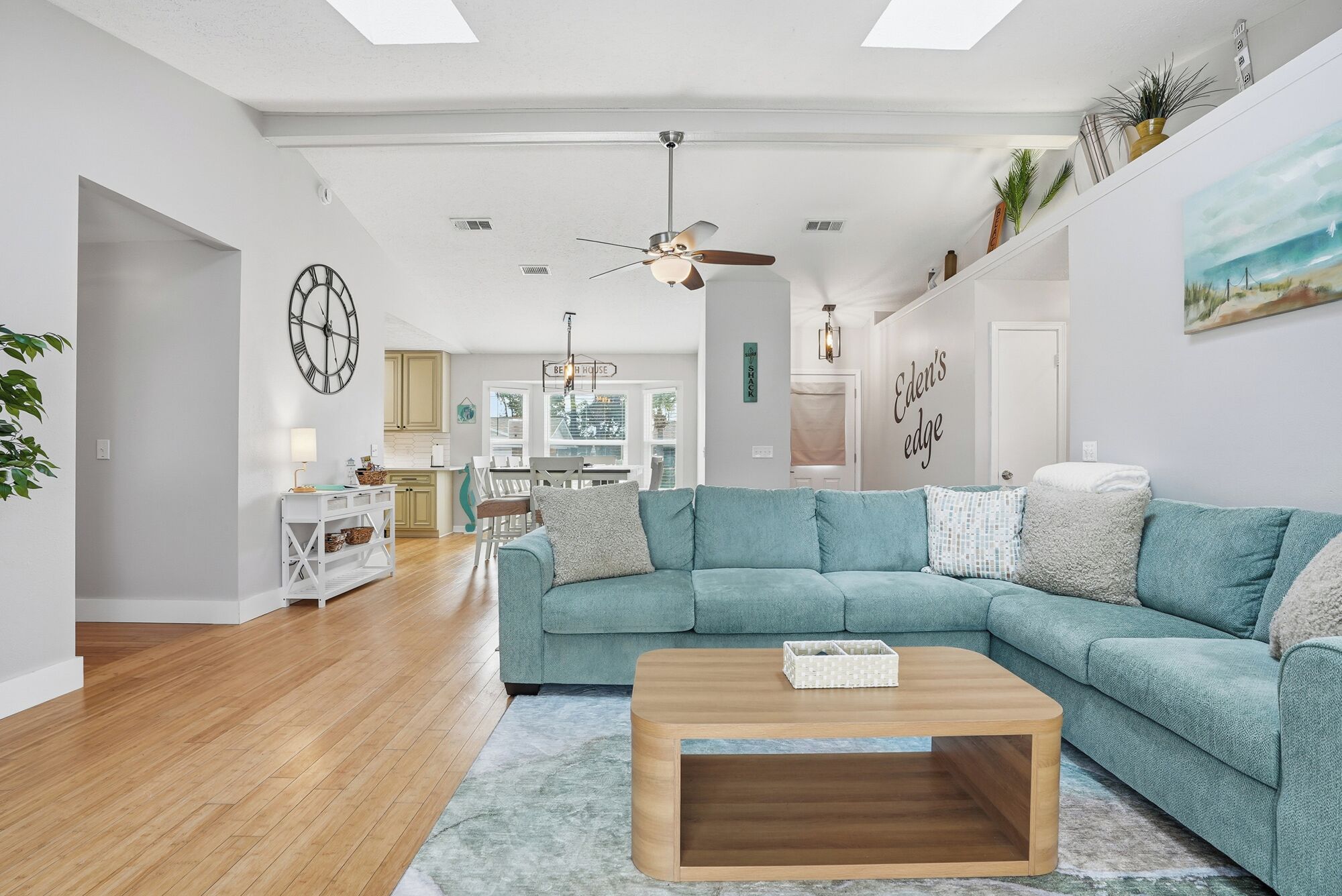 Een moderne woonkamer met een blauwgroene bank, een houten salontafel en een keuken op de achtergrond.
