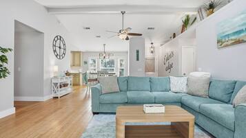 Een moderne woonkamer met een blauwgroene bank, een houten salontafel en een keuken op de achtergrond.