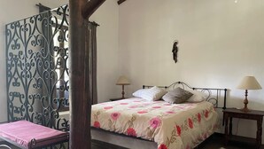 A bedroom with a four-poster bed, two bedside tables with lamps, a chair, and a decorative metal screen.