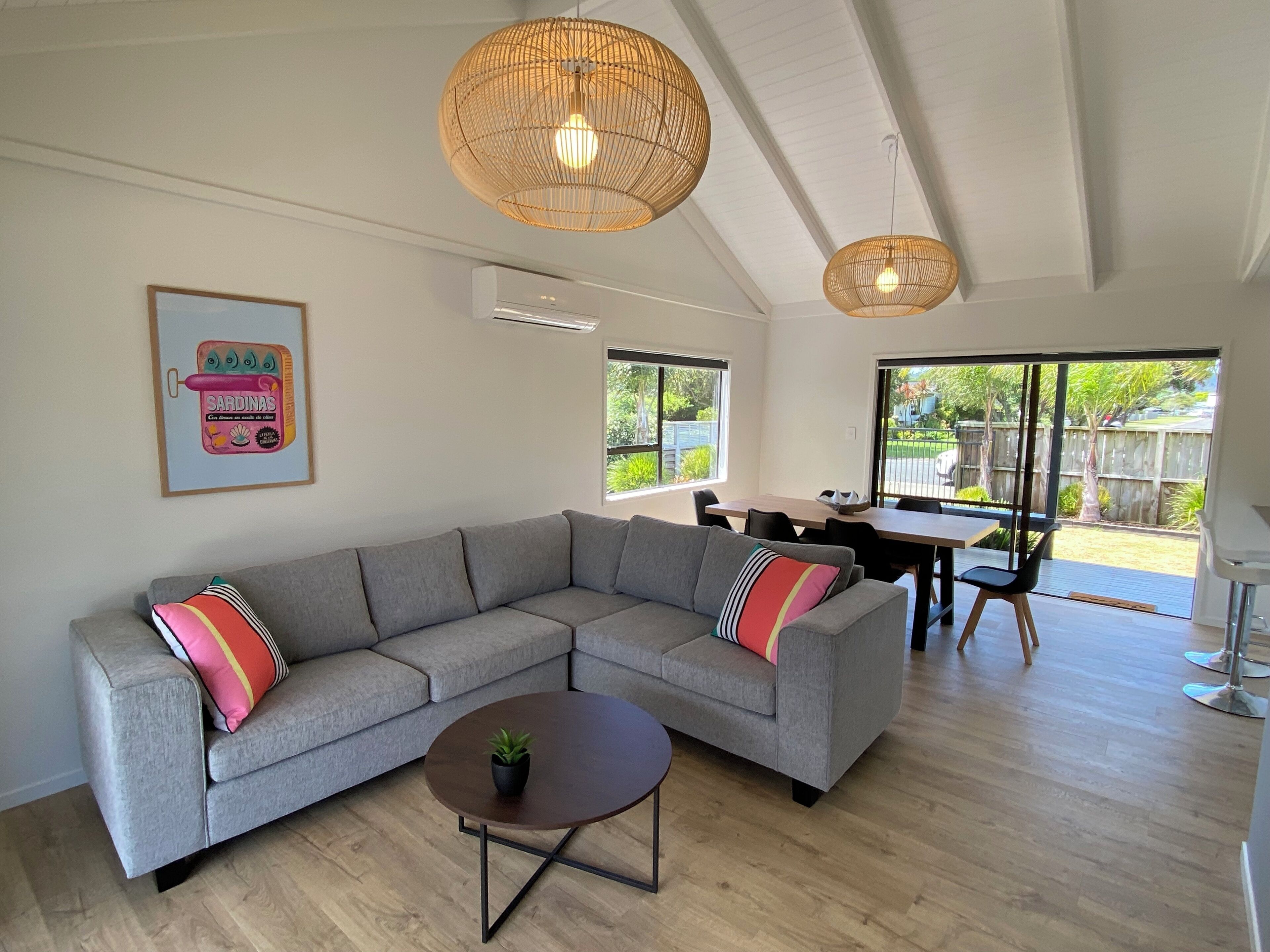 Un salon moderne avec un canapé d’angle gris, une petite table basse ronde et un coin repas comprenant une table et des chaises.