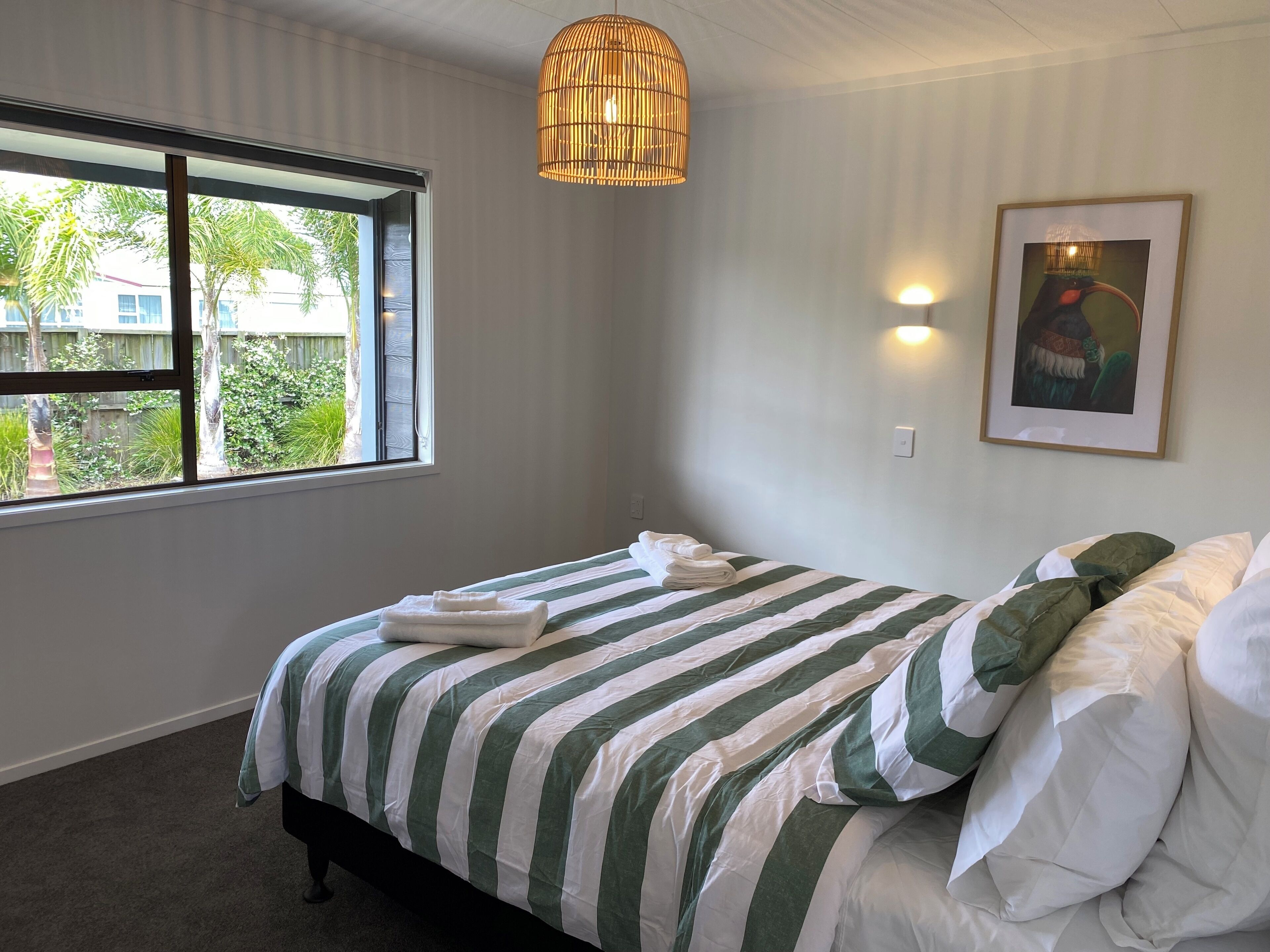 Une chambre à coucher avec un lit, une fenêtre, un luminaire suspendu et un tableau encadré au mur.