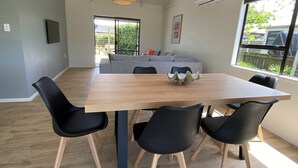 Zona pranzo con tavolo in legno, sedie nere, lampada a sospensione in fibra naturale, divano grigio e finestra con vista su spazi verdi.