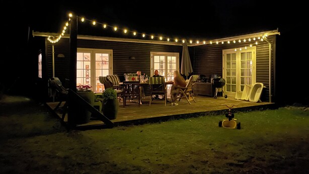 Eine überdachte Terrasse im Freien mit Lichterketten, einem Tisch, Stühlen und einem Grill.