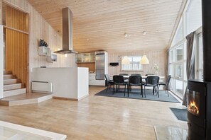 A modern kitchen with wooden cabinetry, a central island, and a dining area with a table and chairs. - Family-friendly holiday home with spa and sauna (Knebel)