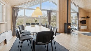 Une pièce chaleureuse avec une grande table ronde, des chaises, une cheminée et de grandes fenêtres.