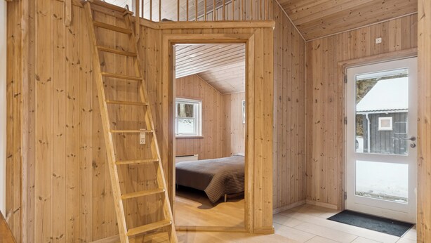 Un intérieur en bois avec une échelle, un lit et une porte donnant sur l’extérieur.