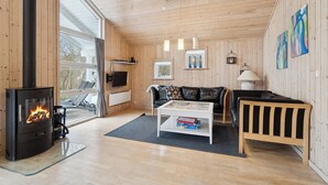 Un salon chaleureux avec un poêle à bois, un canapé en cuir noir, une table basse blanche et un fauteuil en cuir noir.
