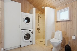 A compact bathroom with a washing machine, a toilet, and a shower stall. - Family-friendly holiday home with spa and sauna (Knebel)