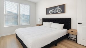 Ein Schlafzimmer mit einem großen Bett, einem Kopfteil mit Beleuchtung, einem Nachttisch, einer Lampe und einem gerahmten Bild von einem Motorrad an der Wand.