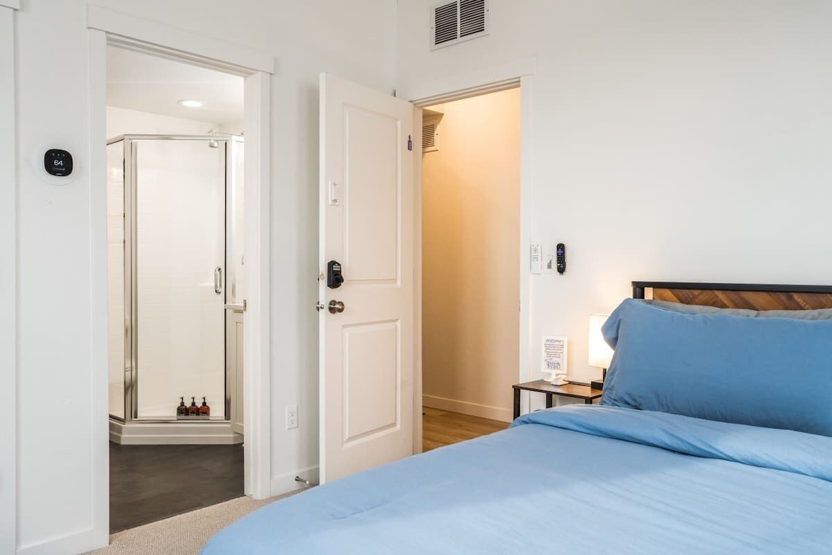 Une chambre d’hôtel comprenant un lit, une table de chevet, une lampe, une porte et un espace douche.