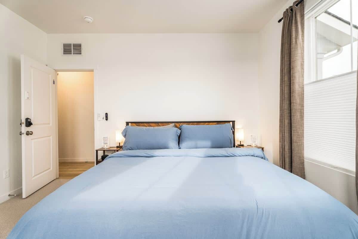 A bedroom with a large bed, a wooden headboard, bedside tables with lamps, and a window with curtains.