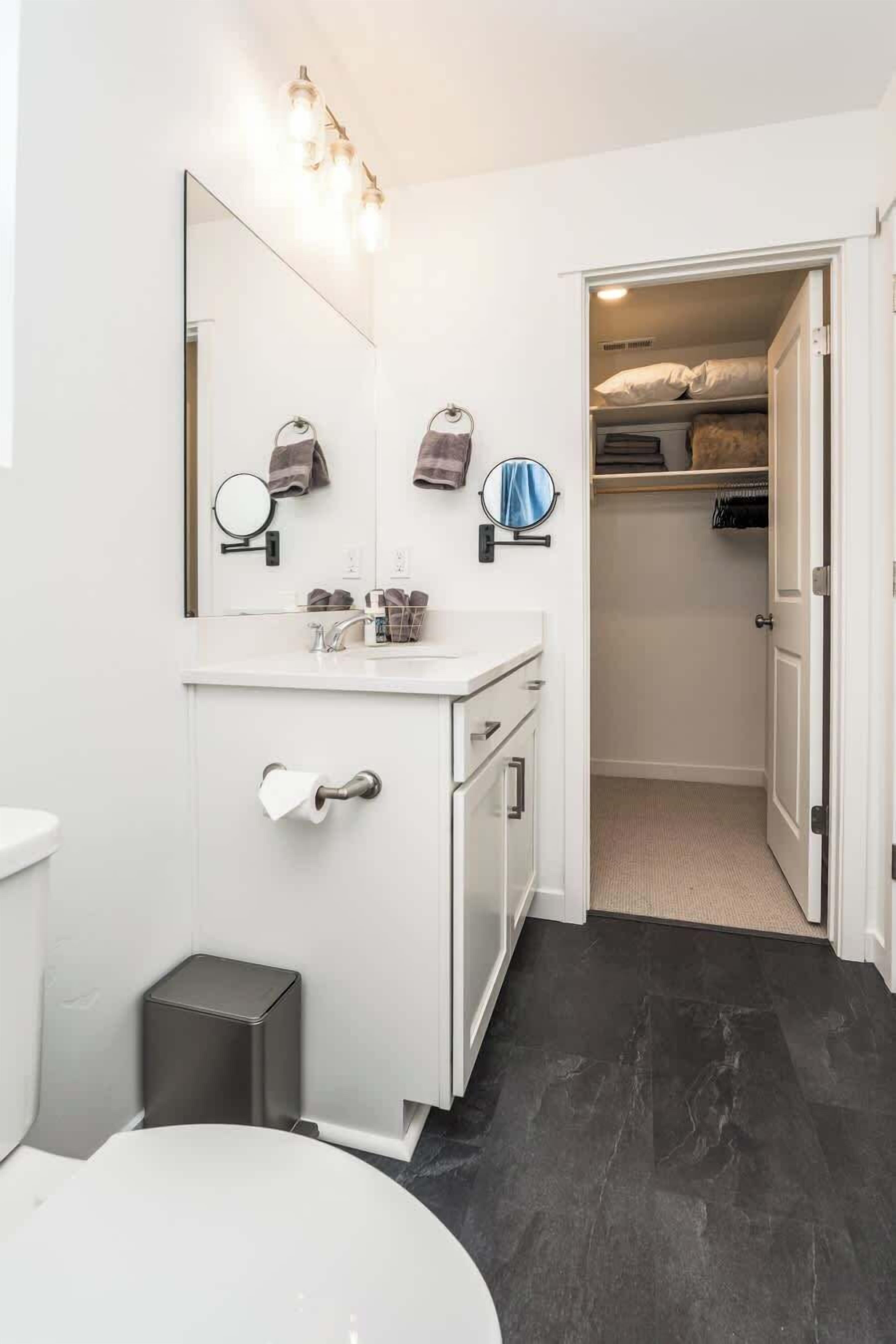 Une salle de bain moderne avec un meuble-lavabo blanc, un miroir et des toilettes. On y trouve une petite poubelle et un porte-serviettes.