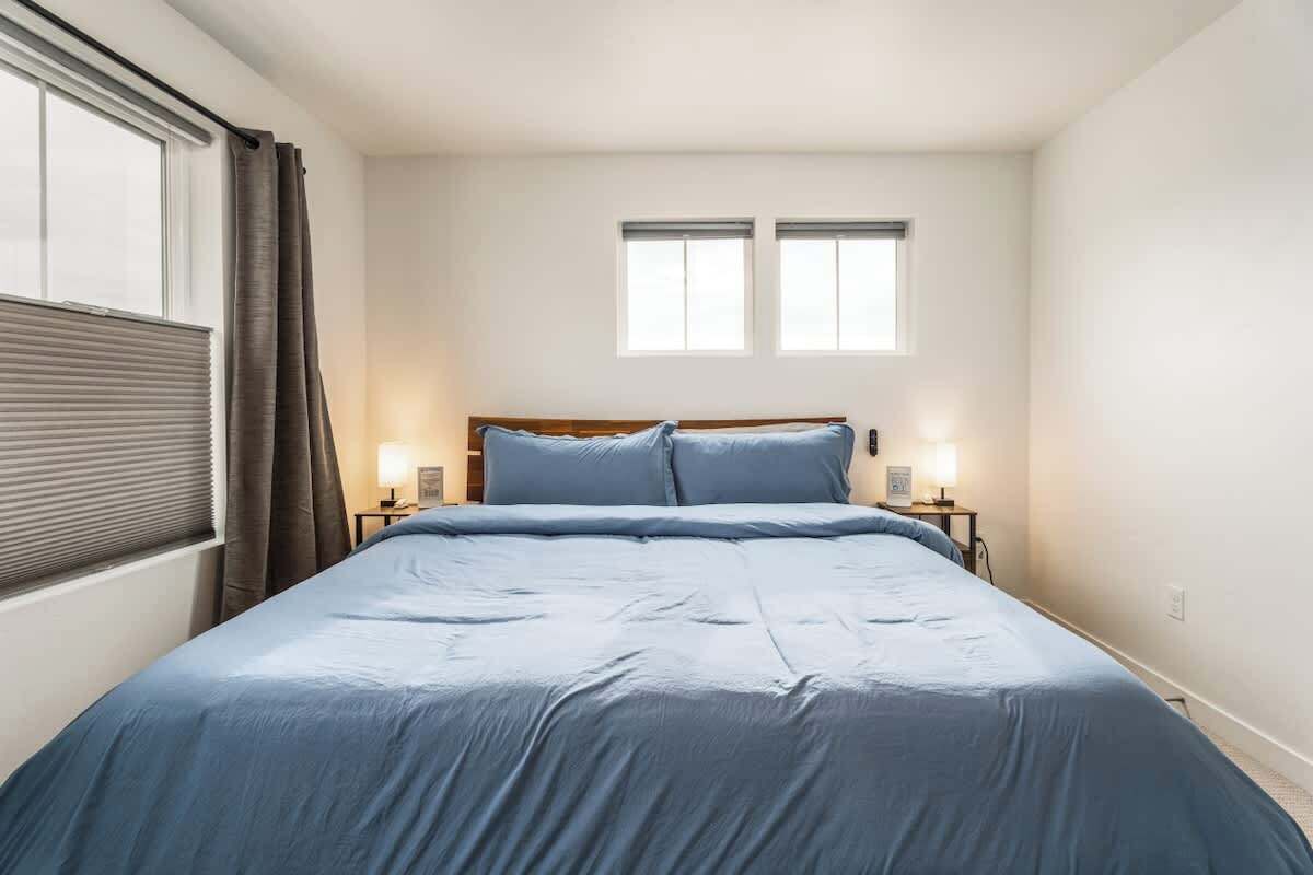 A bedroom with a bed, two bedside tables, a window with curtains, and a wall-mounted light fixture.