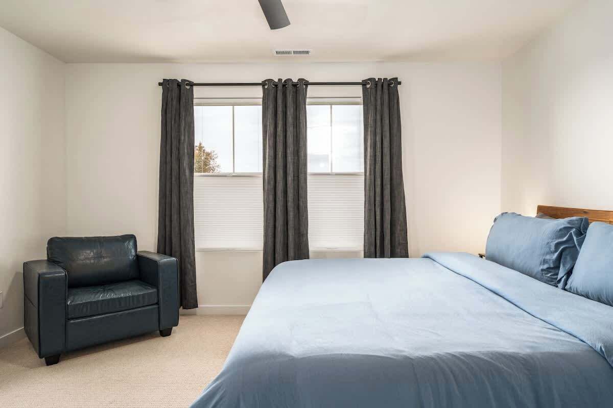 Un dormitorio con cama, una silla y una ventana con cortinas.
