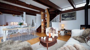 A spacious living area with a high ceiling, wooden beams, a fireplace, a dining area with a Christmas tree, and a cozy seating arrangement.